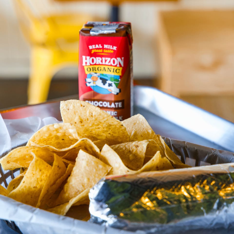 Crispy tortilla chips and green dip sit in foil trays beside a Horizon Organic chocolate milk carton.